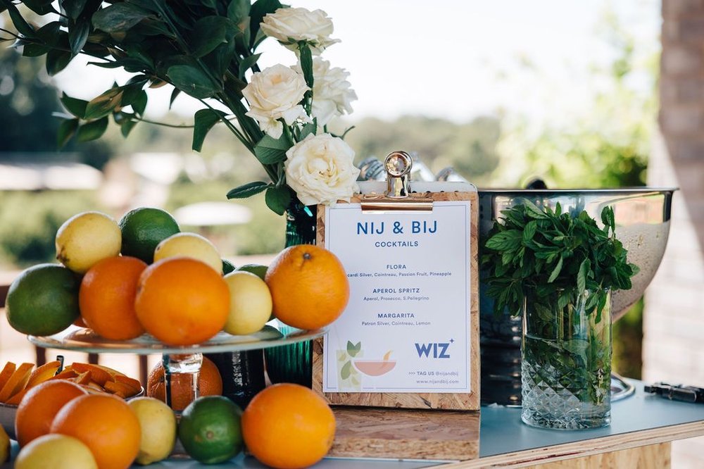 Styled bar cart detail with a NIJ & BIJ cocktail menu card, fresh citrus, and mint in a vase