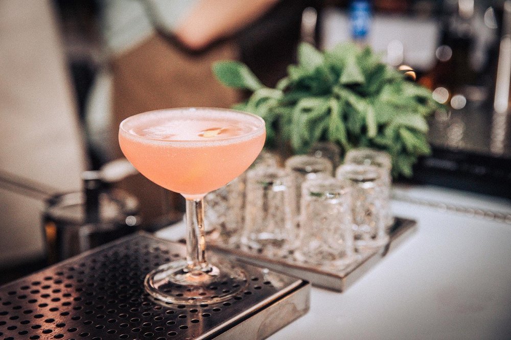 Bartender straining a cocktail into chili-salt-rimmed coupe glasses